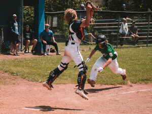 Player running home with catcher jumping to catch ball.